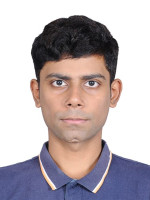 A young man with short dark hair faces the camera, wearing a blue shirt.