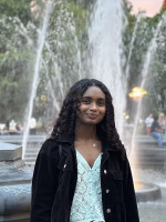 Headshot of a person in front of a fountain. The person is well-lit and in focus, with the water flowing blurred in the background.